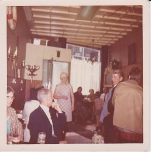 Gezellige drukte op de zondagmiddag. Aan de tafel bij het raam zit rechts Wim Mackaay (de sportvisser) met Piet Scholte en zijn vrouw, allen uit de Gorzenwijk. De man met zijn rug naar de bar is buurman Gerrit van den Broek. Tussendoor loopt tante Lena te bedienen.